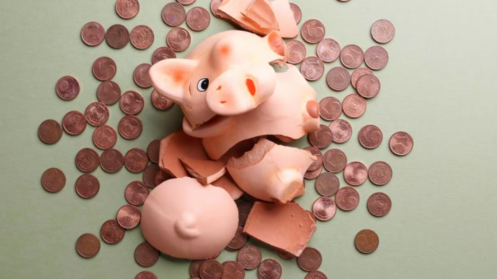 An image of a smashed pink ceramic piggy bank on a pale green surface with dozens of one cent coins spilled out across it. 