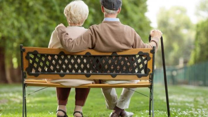 Two older people sitting on a bench, viewed from the back.