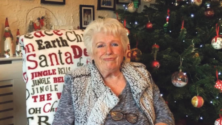 A photo of Noelle, Community Hero of 2020, sitting by a Christmas tree.