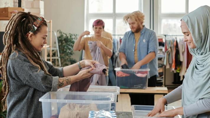 A group of four people sort clothing into large plastic containers on trestle tables.