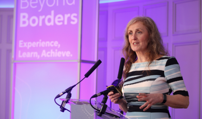 An image of Grainne Berrill speaking from a lectern at a Beyond Borders event. 