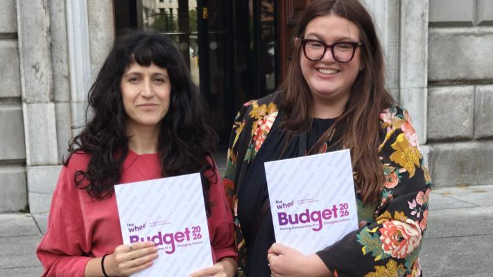Two women dressed each holding a copy of The Wheel's prebudget submission standing side bide side in front of Leinster House in Dublin.