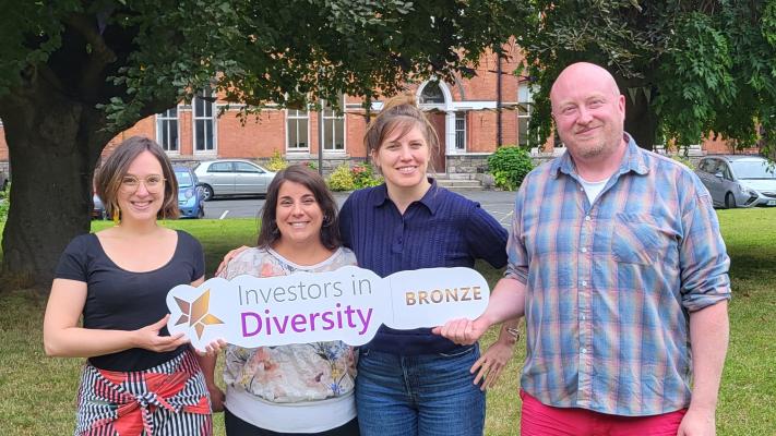 Four people holding a banner for the Irish Centre for Diversity's Bronze Accreditation standing on a lawn in front of a large tree.