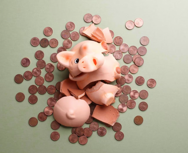 An image of a smashed pink ceramic piggy bank on a pale green surface with dozens of one cent coins spilled out across it. 