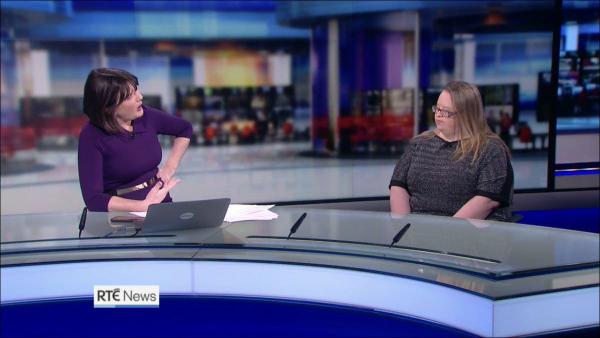 A woman with blind hair and glasses being interviewed in a national news studio by another woman with dark hair in a dark purple dress.