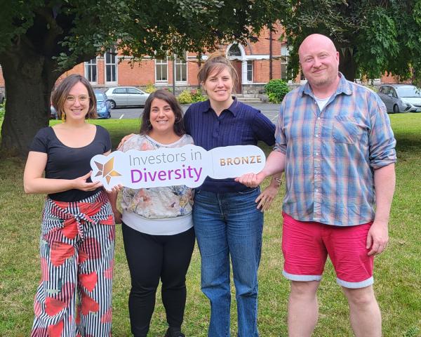 Four people holding a banner for the Irish Centre for Diversity's Bronze Accreditation standing on a lawn in front of a large tree.