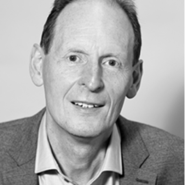 A man with short hair is wearing a collared shirt and blazer. He is looking at the camera and smiling slightly. The photo is black and white with a plain background.