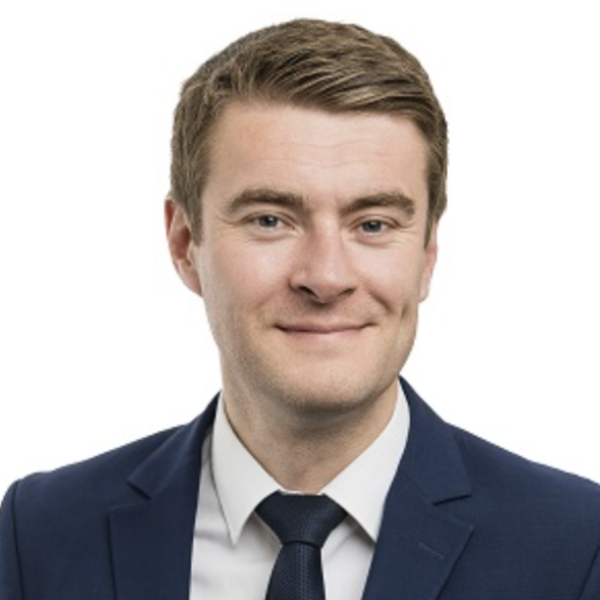 A man in a navy blue suit, white shirt, and dark tie poses for a headshot against a plain white background. He has short brown hair, light skin, and a slight smile.