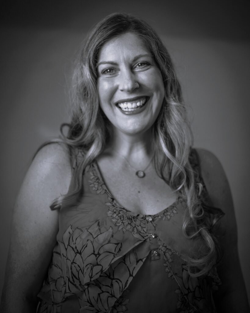 A portrait of a smiling woman with long hair wearing a floral blouse.