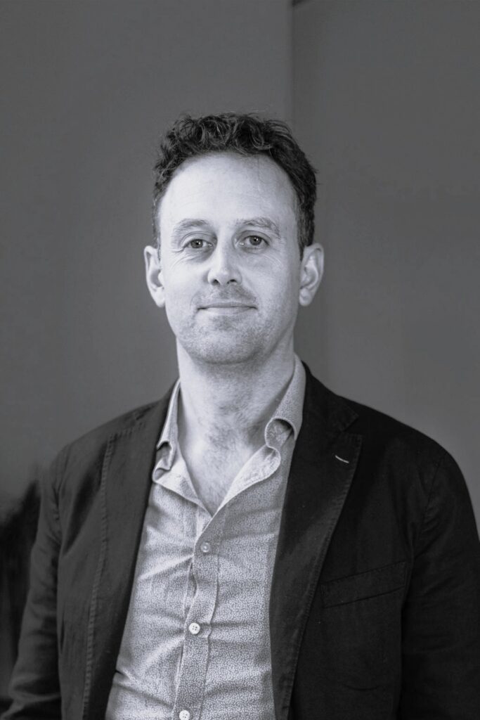 A middle-aged man in a collared shirt and jacket looking at the camera.