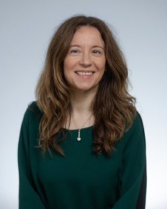 Woman with long brown hair wearing a green jumper and a long necklace.