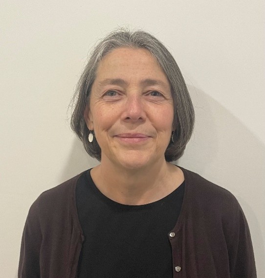 A middle-aged woman with shoulder-length grey hair wearing a black shirt and dark cardigan.