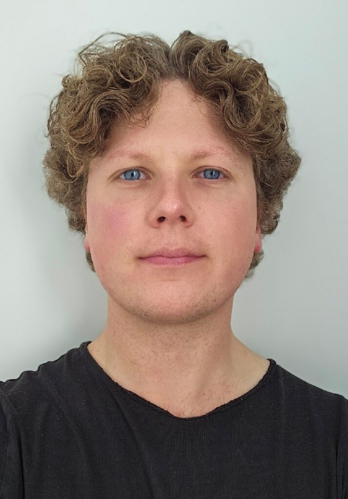 Headshot of a person with curly light brown hair and blue eyes looking directly at the camera.